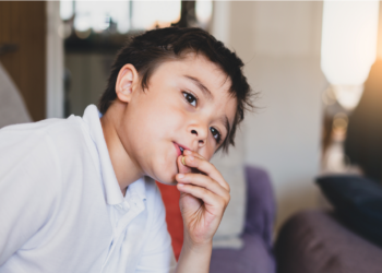 A kid looks sad as his fingers touch the lips.