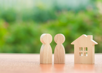 A wooden house model stands with a wooden carved-out couple.