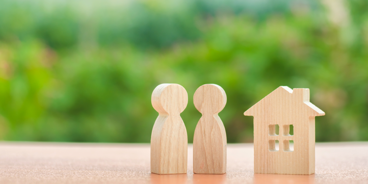 A wooden house model stands with a wooden carved-out couple.