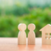 A wooden house model stands with a wooden carved-out couple.