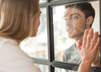 A man looks through a glass at her partner.