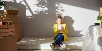 A woman loos pensive while sitting amid the boxes.