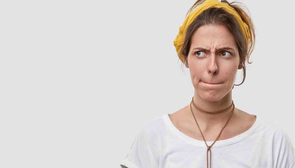 woman keeps lips pressed, has frustrated facial expression, frowns face in displeaure