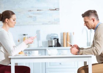 A couple uses mobile phones while sitting on a table.