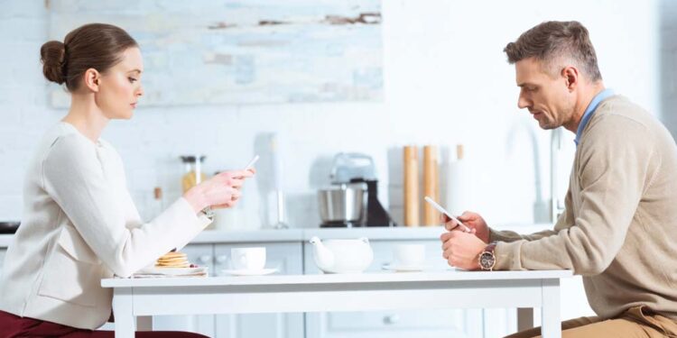 A couple uses mobile phones while sitting on a table.