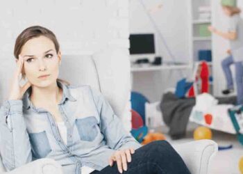 Worried mother relaxing on armchair while her son plays inthe background