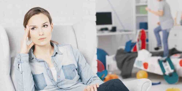 Worried mother relaxing on armchair while her son plays inthe background